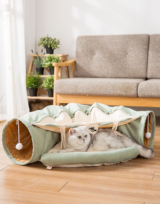 Cat lying on a green pet bed with tunnel in a living room setting