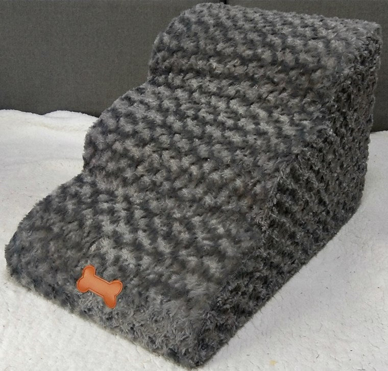 Gray textured pet bed with a small orange dog-shaped tag on a white surface.