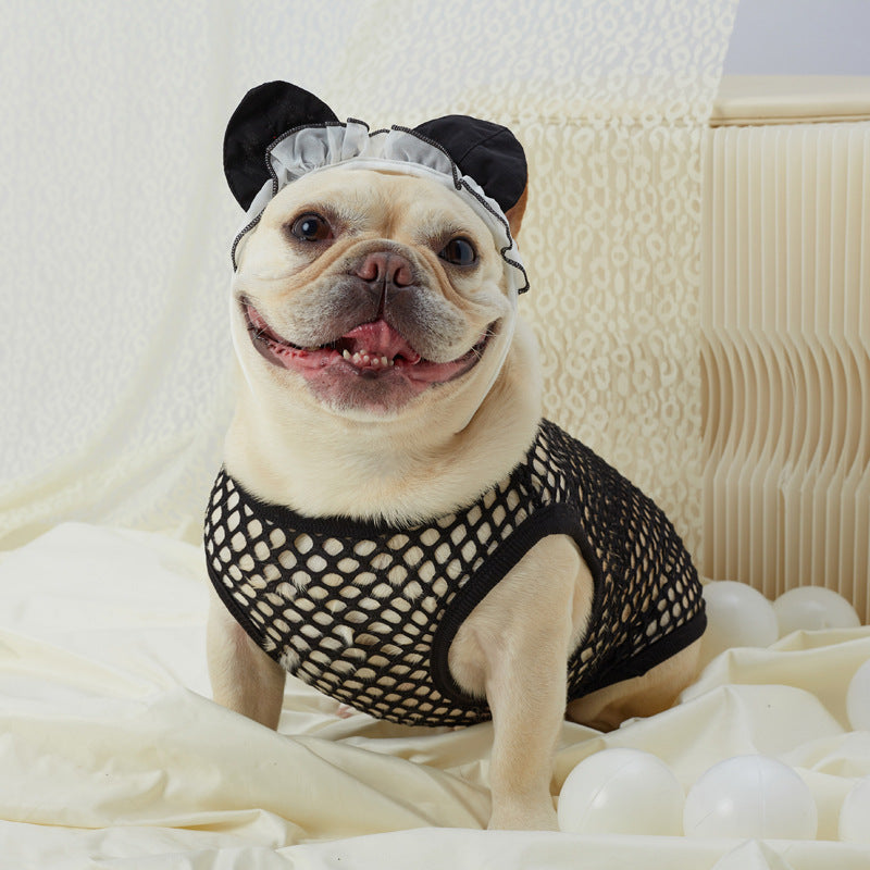 Dog wearing a black fishnet harness and headband with white polka dots on a soft surface.