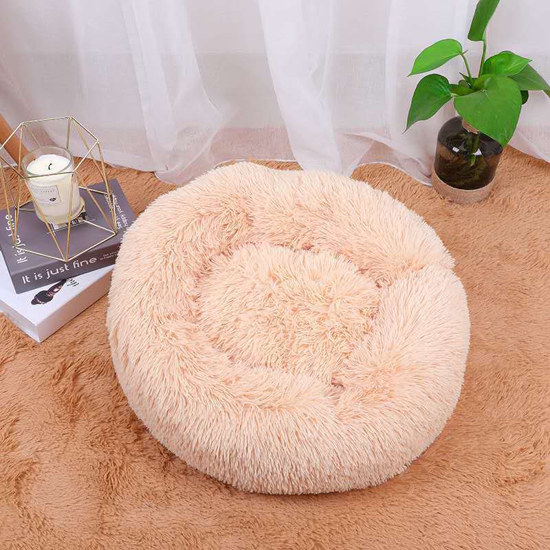 Round fluffy beige cushion on a brown rug with a white curtain and plant in the background