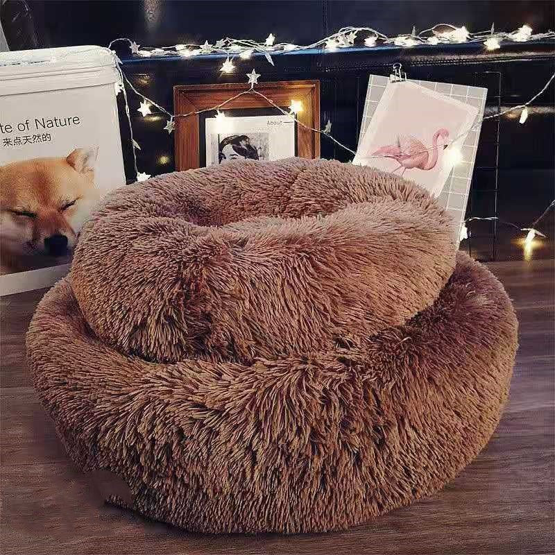 Fluffy brown pet bed on a wooden floor with decorative lights and photos in the background.