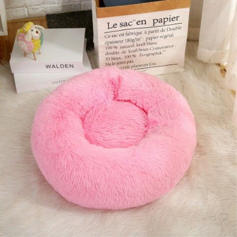 Pink donut-shaped pet bed on a light wooden floor with books in the background.