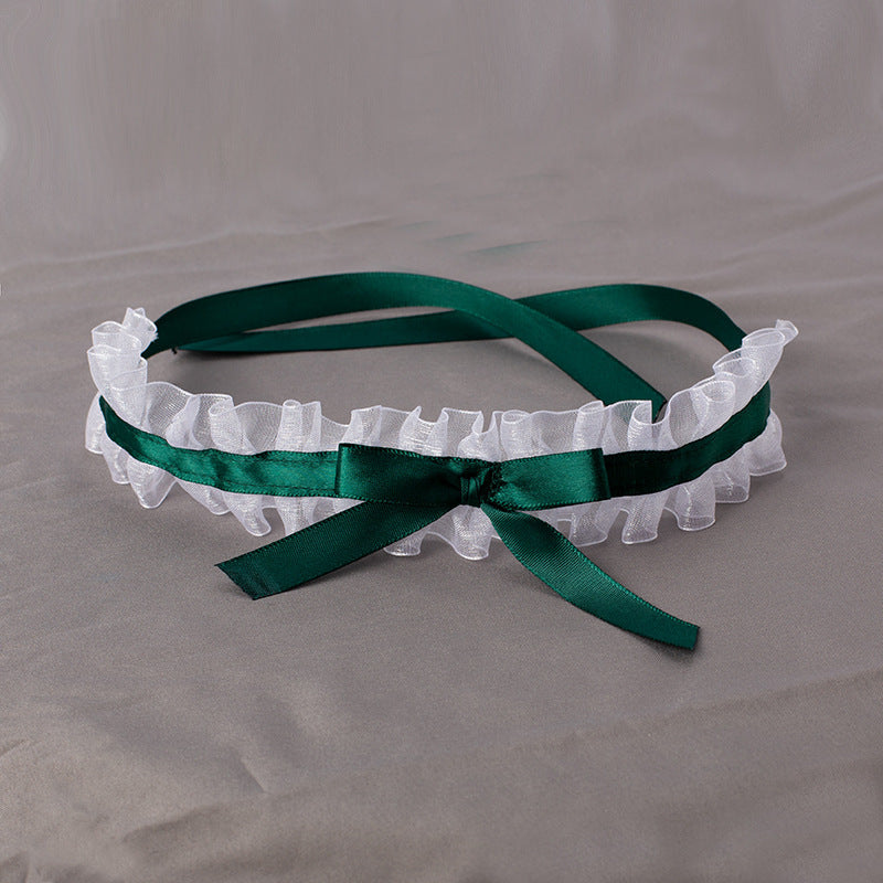 White lace headband with a green ribbon on a gray background